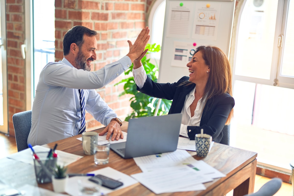 Deux personnes qui se félicitent autour d’une table de travail, illustration du conseil.